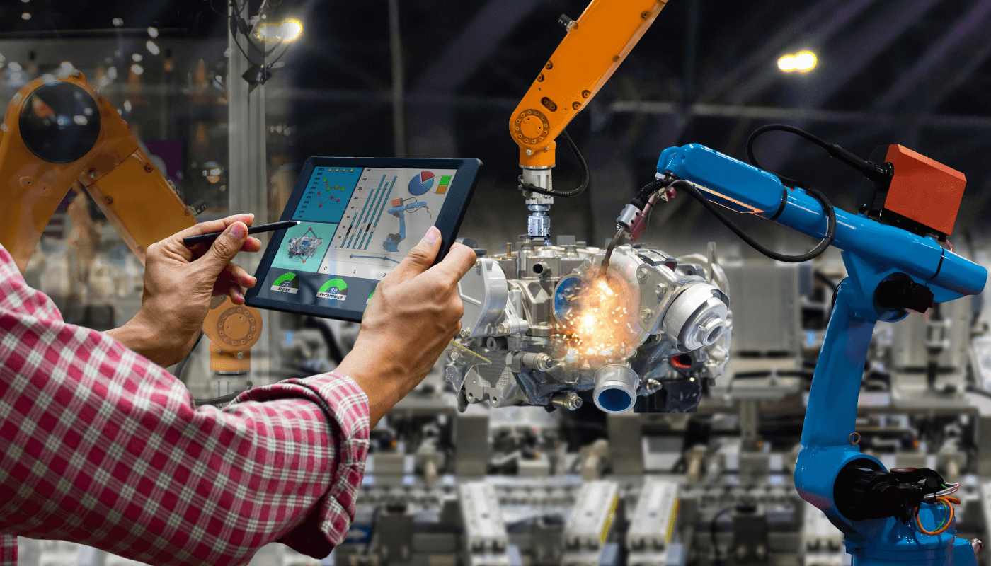 An engineer using the touchscreen of a mobile tablet to control a robot on a manufacturing floor.