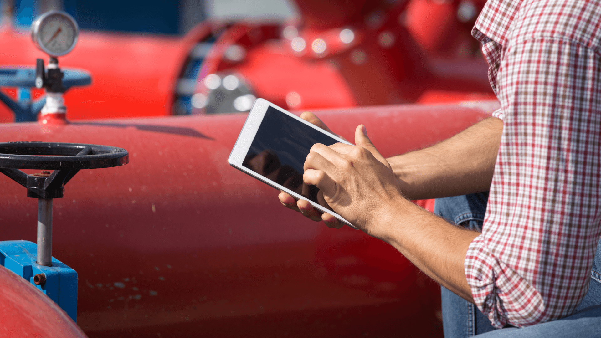 A man in a flannel shirt using an ipad to check data at a pipeline with a valve. (1)