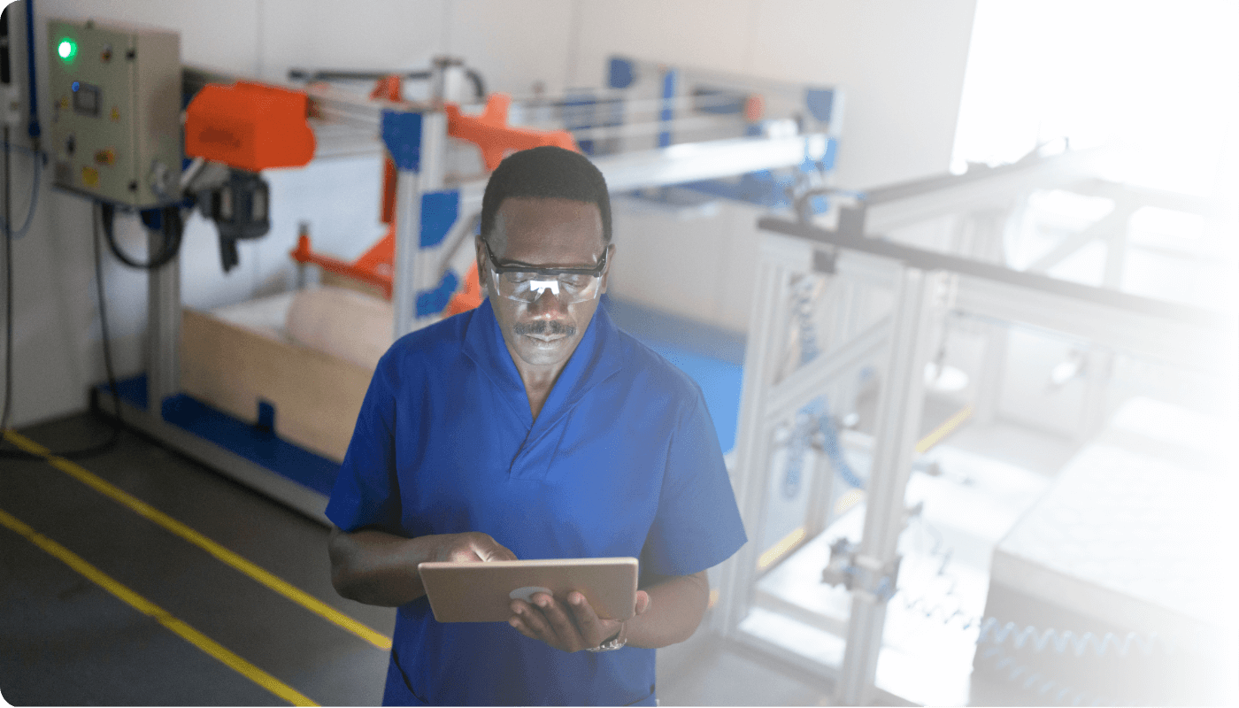 An industrial worker wearing blue scrubs inside a factory using an ipad to look at data and automate task. (2) (1)