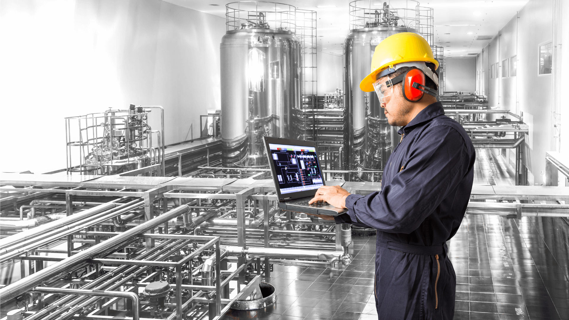 A worker wearing safety goggles, a helmet, and ear protection, using a computer running PI Vision software (1)