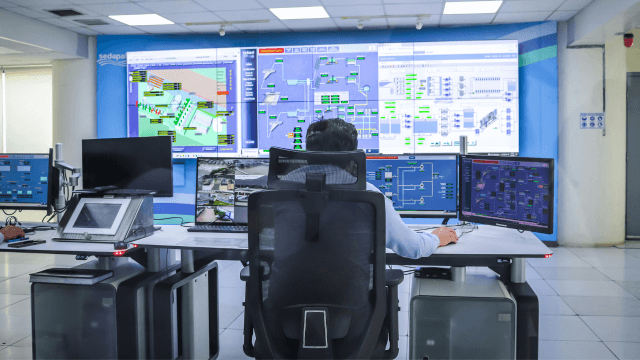 A person sitting at a desk with multiple monitors, using it to monitor the infrastructure of a computer system (1)