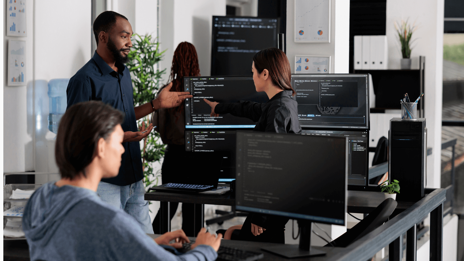 A diverse group of software engineers viewing source code on multiple computer screens in an office