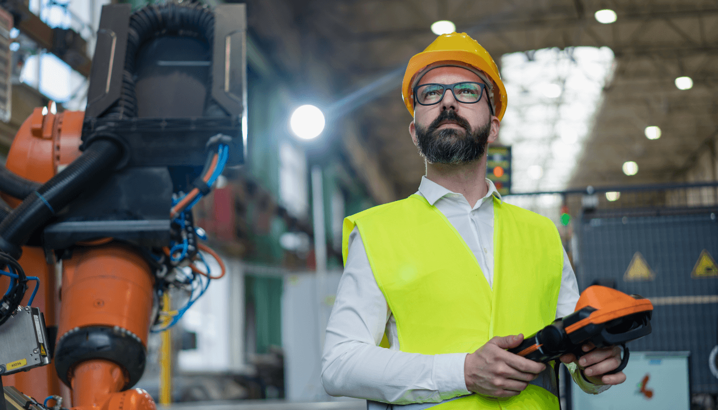 Worker with an orange hard hat and yellow vest installing hardware on equpiment.