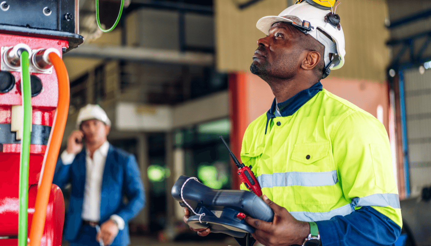 Industrial worker checking equipment with his project manager in the background