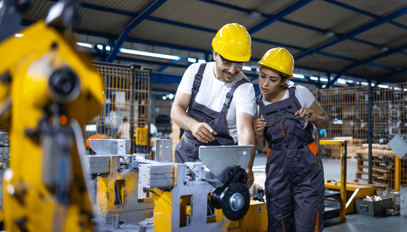 Two workers in yellow hard hats working on equipment in a manufacturing warehouse