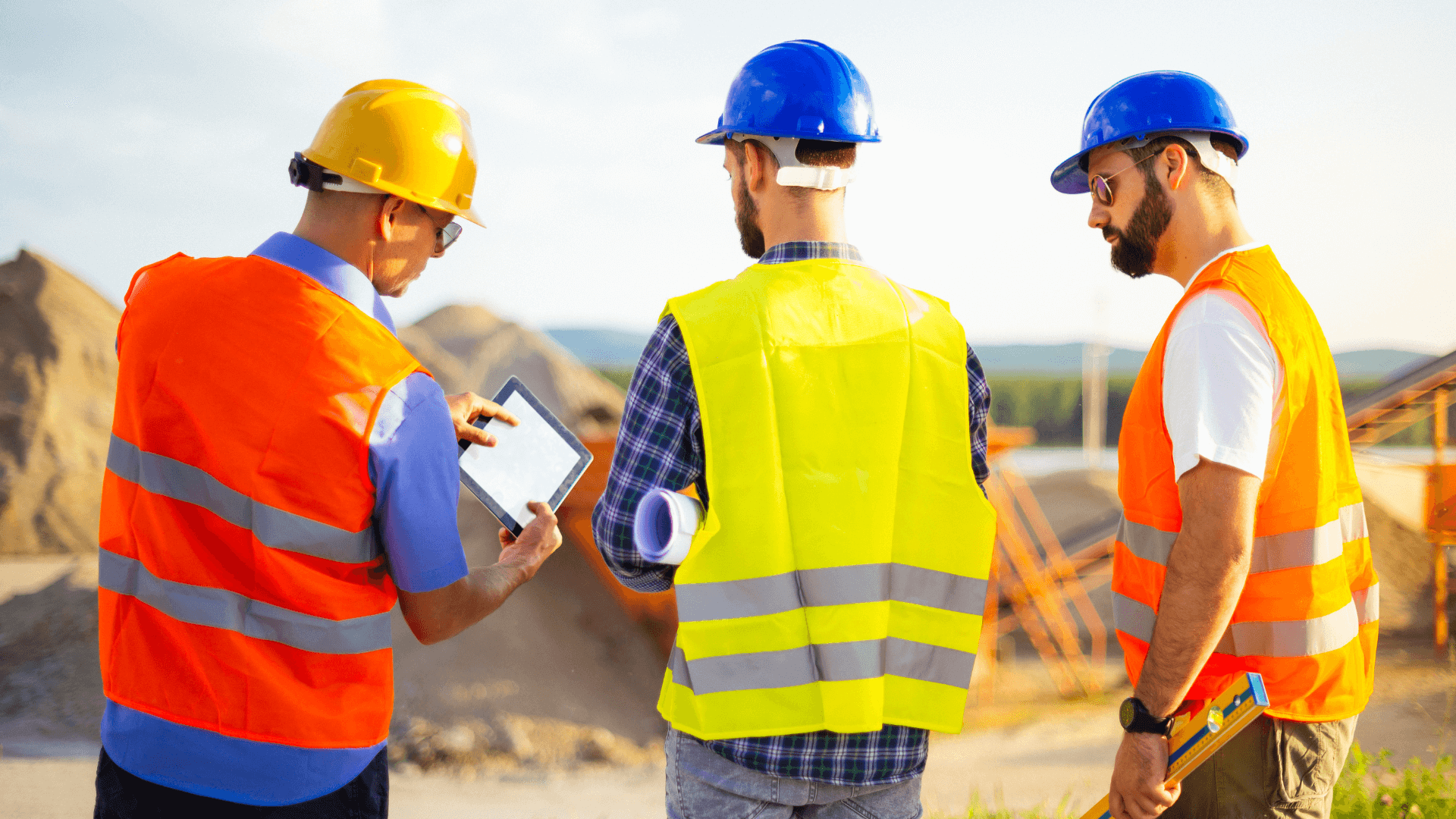 Three workers at some type of construction site, one of the workers is holding an ipad  (1)