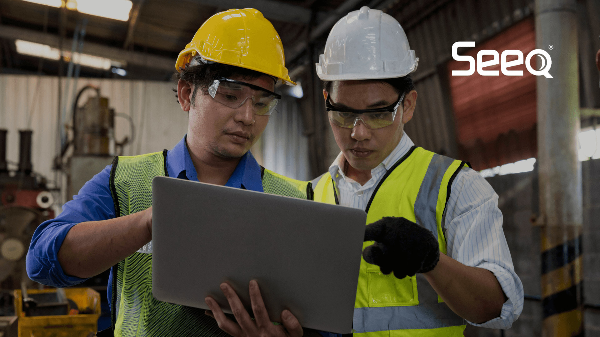 two industrial workers with hard hats looking at data on a laptop (1)